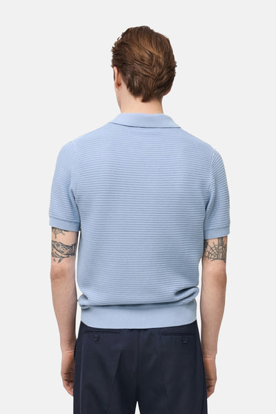 Polo bleu à manches courtes de MANGO, avec une texture nid d'abeille, porté avec un pantalon bleu marine.