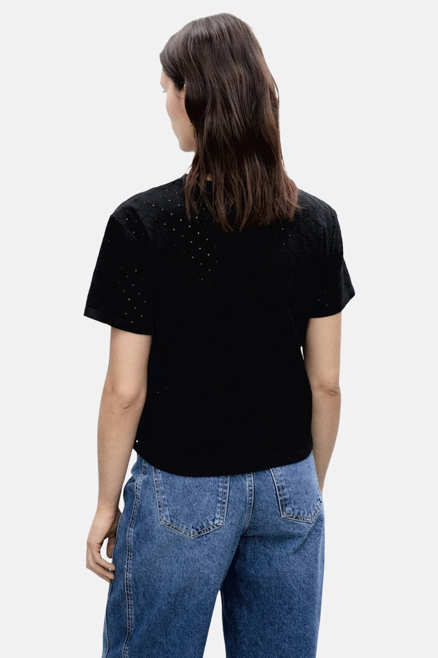 T-shirt noir à manches courtes de MANGO, avec motifs perforés, porté avec un jean bleu ample.
