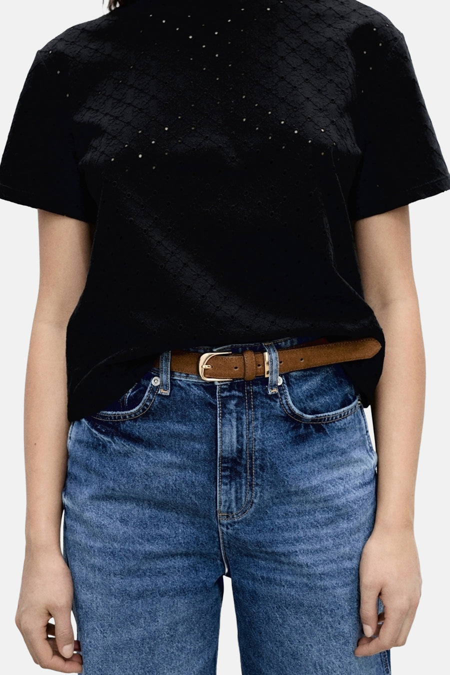 T-shirt noir à manches courtes de MANGO, avec un motif ajouré et porté avec une ceinture marron et un jean bleu.
