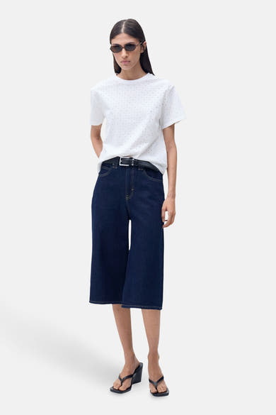 T-shirt blanc à manches courtes de MANGO, avec motif à pois discrets, porté avec un pantalon large et des lunettes de soleil.