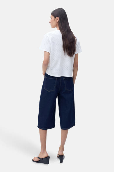 T-shirt blanc à manches courtes de MANGO, avec un motif à pois, porté avec un pantacourt en jean foncé.