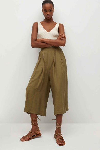 Olijfgroene wijde broek van MANGO met plooien, gedragen met een witte tanktop en sandalen met veters.