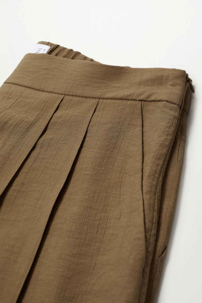 Pantalon marron en lin par MANGO, avec des plis plats sur le devant et une texture froissée.