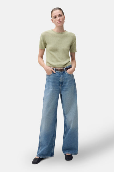 Pull à col rond vert de MANGO, porté avec un jean ample et une ceinture marron.