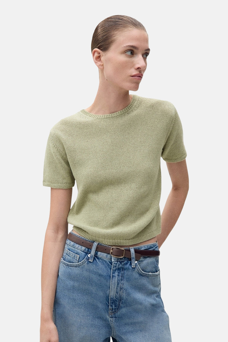 Pull à col rond vert de MANGO, avec texture tricotée, porté avec un jean taille haute et une ceinture marron.
