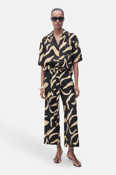 Pantalon noir à motif ondulé van MANGO, porté avec ceinture assortie et chaussures à talons hauts.
