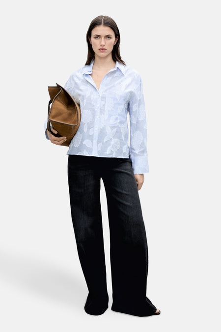 Blauwe blouse met lange mouwen van MANGO, met wit bloemenpatroon, gedragen met een wijde zwarte broek.