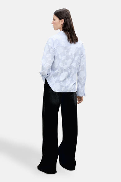 Blauwe blouse met lange mouwen van MANGO, met getextureerd bloemenpatroon, gedragen met een wijde zwarte broek.
