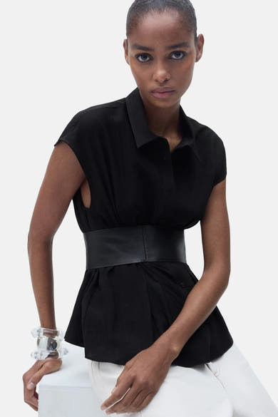 Zwarte blouse met korte mouwen van MANGO, met ceintuur in de taille en witte broek.