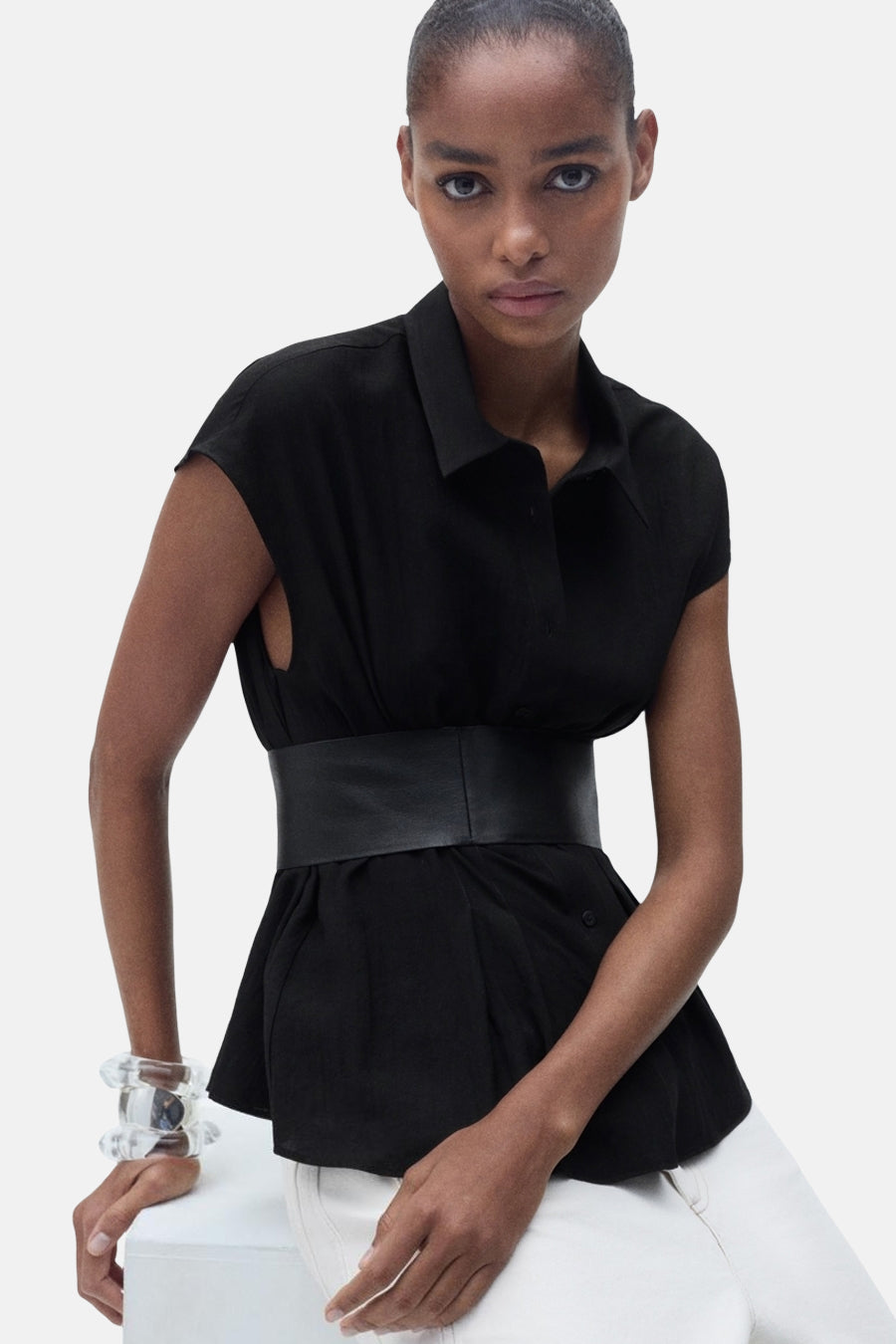 Zwarte blouse met korte mouwen van MANGO, met ceintuur in de taille en witte broek.
