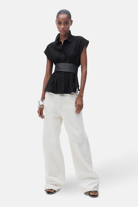 Zwarte blouse met korte mouwen van MANGO, gedragen met een brede riem, een witte broek en sandalen.