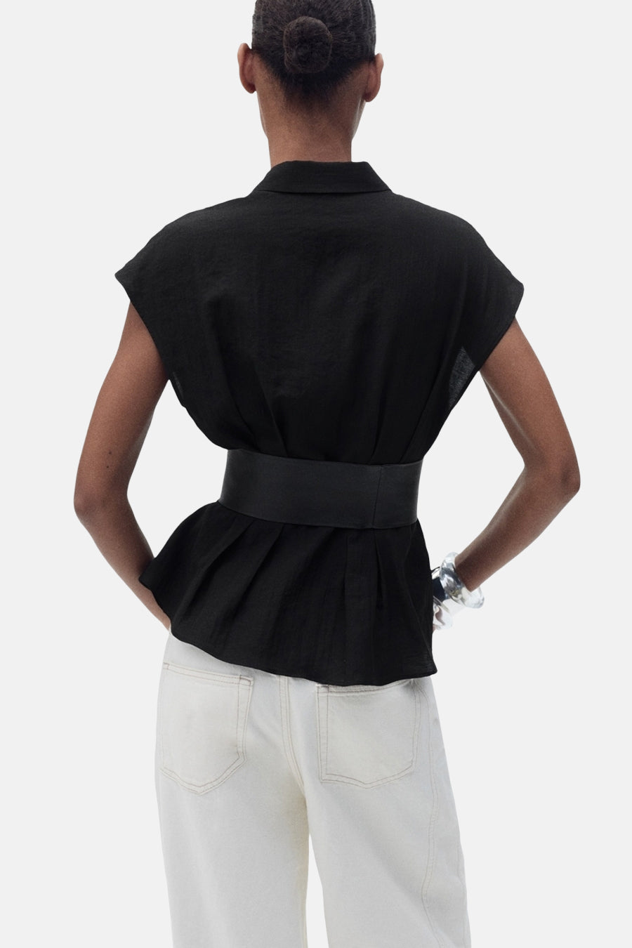 Chemisier noir à manches courtes de MANGO, avec ceinture à la taille et pantalon blanc.