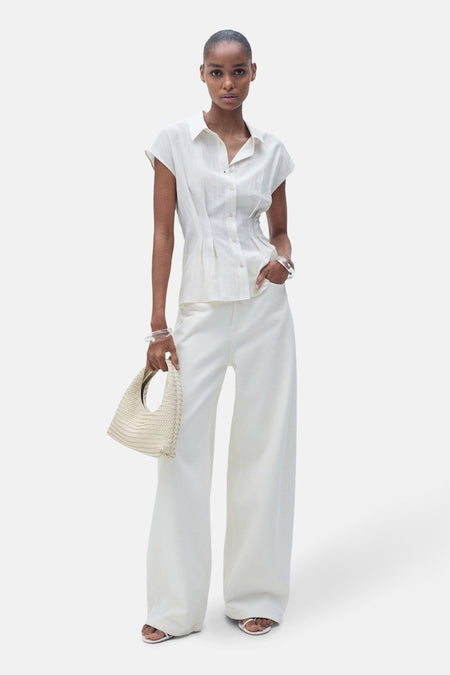 Ecru blouse met korte mouwen van MANGO, met een getailleerde pasvorm en gedragen met een wijde witte broek.