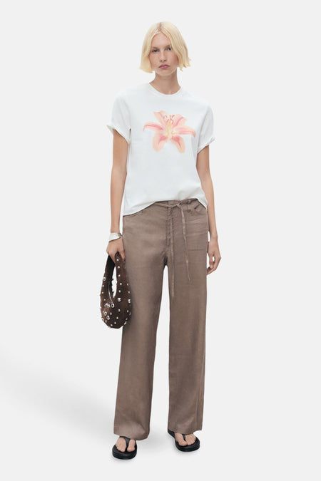 T-shirt à manches courtes blanc à imprimé floral, de MANGO, porté avec un pantalon marron clair et des sandales noires.
