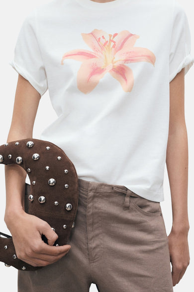 Wit T-shirt met korte mouwen van MANGO met roze bloemenprint, gedragen met een bruine broek en een tas met studs.