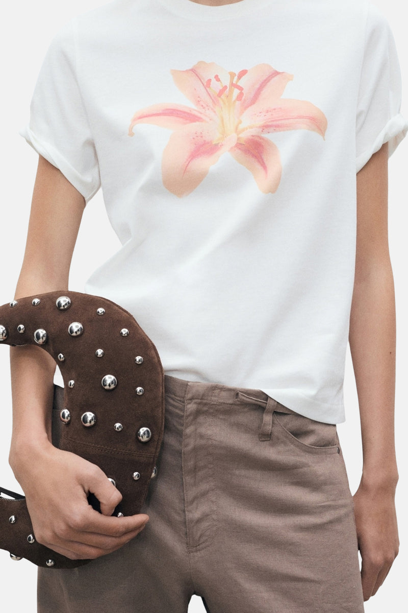 Wit T-shirt met korte mouwen van MANGO met roze bloemenprint, gedragen met een bruine broek en een tas met studs.