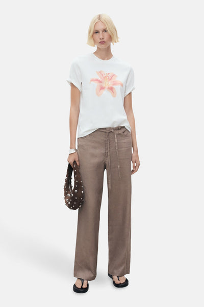 Wit T-shirt met korte mouwen van MANGO, versierd met een perzikbloemenpatroon, gedragen met een bruine broek en zwarte sandalen.