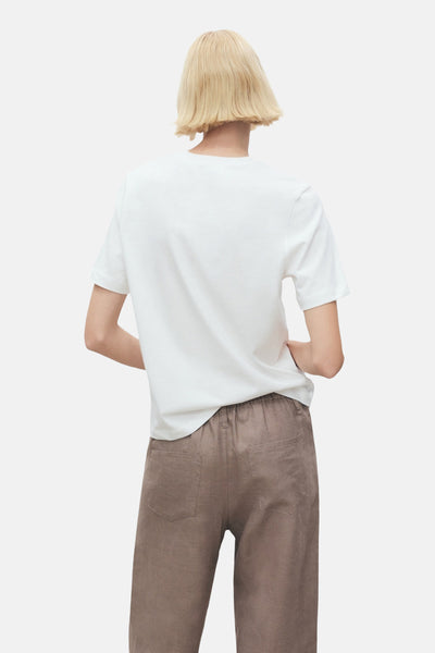 T-shirt blanc à manches courtes de MANGO, porté avec un pantalon décontracté couleur terre, vue de dos.
