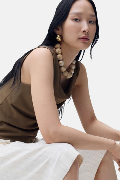 Débardeur brun de MANGO avec encolure drapée, porté avec un collier de perles et des boucles d'oreilles dorées.