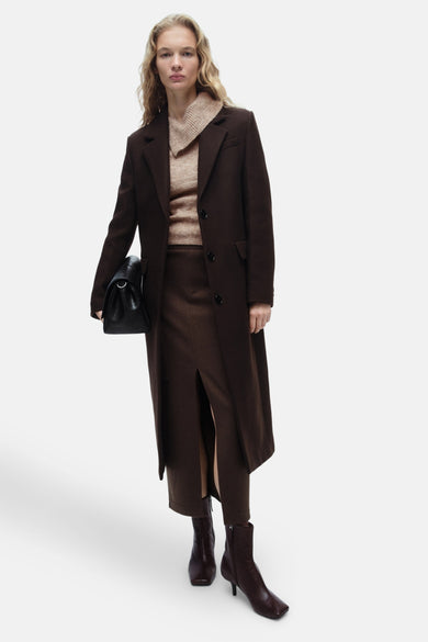 Beige gerollde kraagpull-over van MANGO, gedragen met een lang bruine jas en een passende rok.