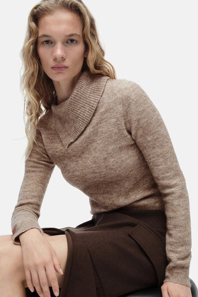 Pull à col roulé beige de MANGO, porté avec une jupe marron, cheveux blonds ondulés.