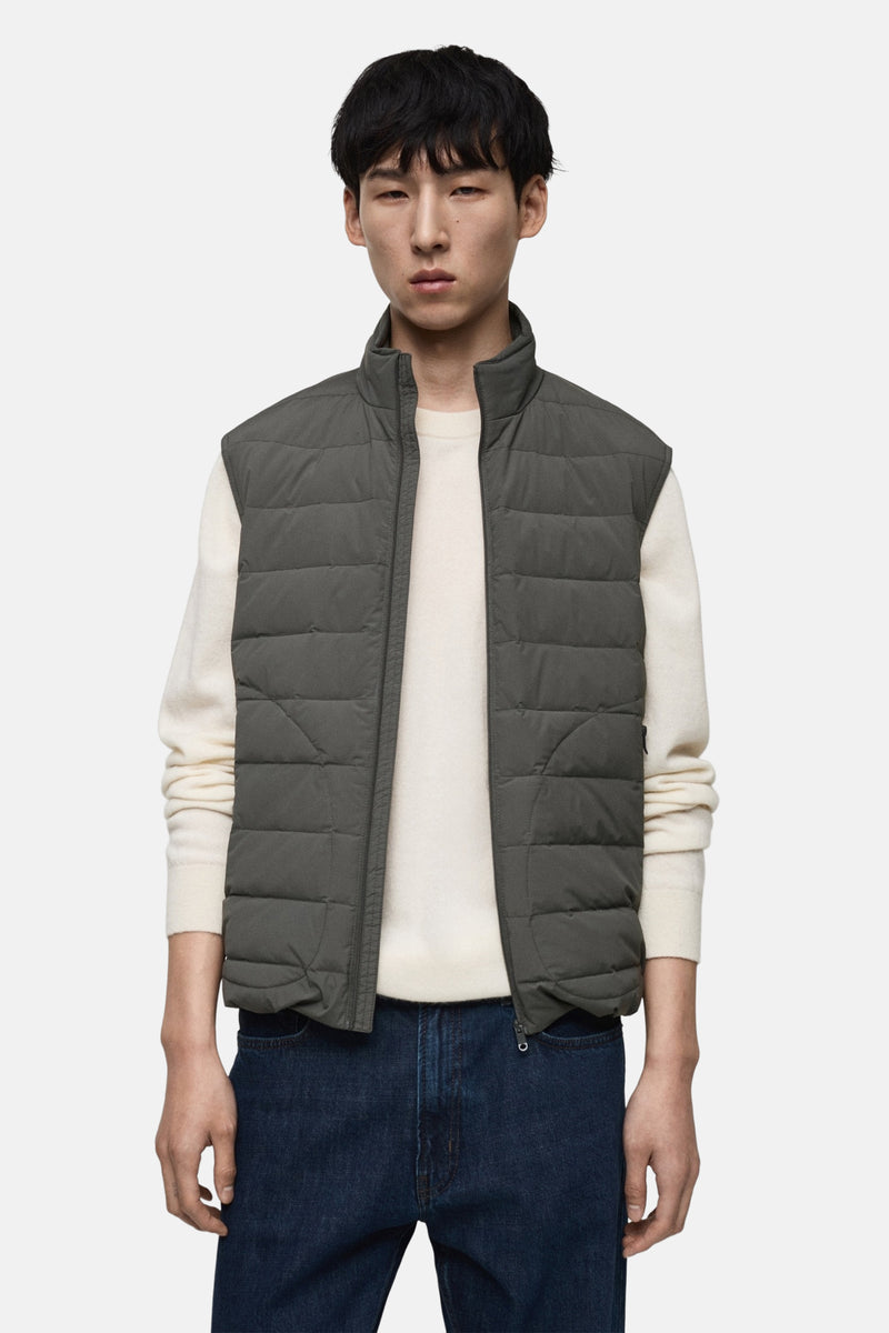Grijze mouwloze jas van MANGO, gedragen over een crèmekleurige trui en donkerblauwe jeans, van achteren gezien.