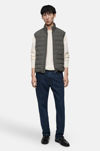 Grijze mouwloze jas van MANGO, gedragen over een crèmekleurige trui en donkerblauwe jeans, met zwarte schoenen.
