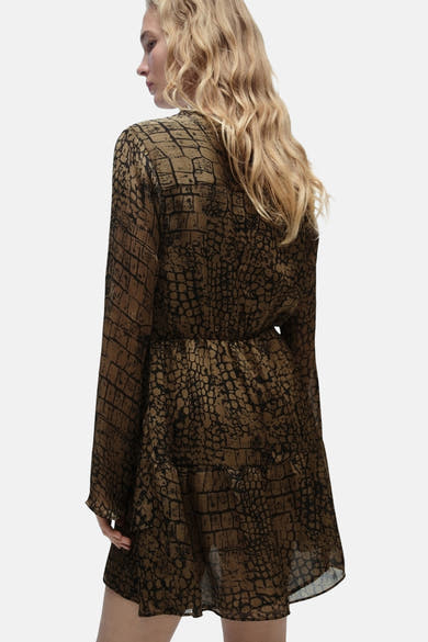 Kaki jurk met lange mouwen van MANGO, krokodillenprint op een beige achtergrond.