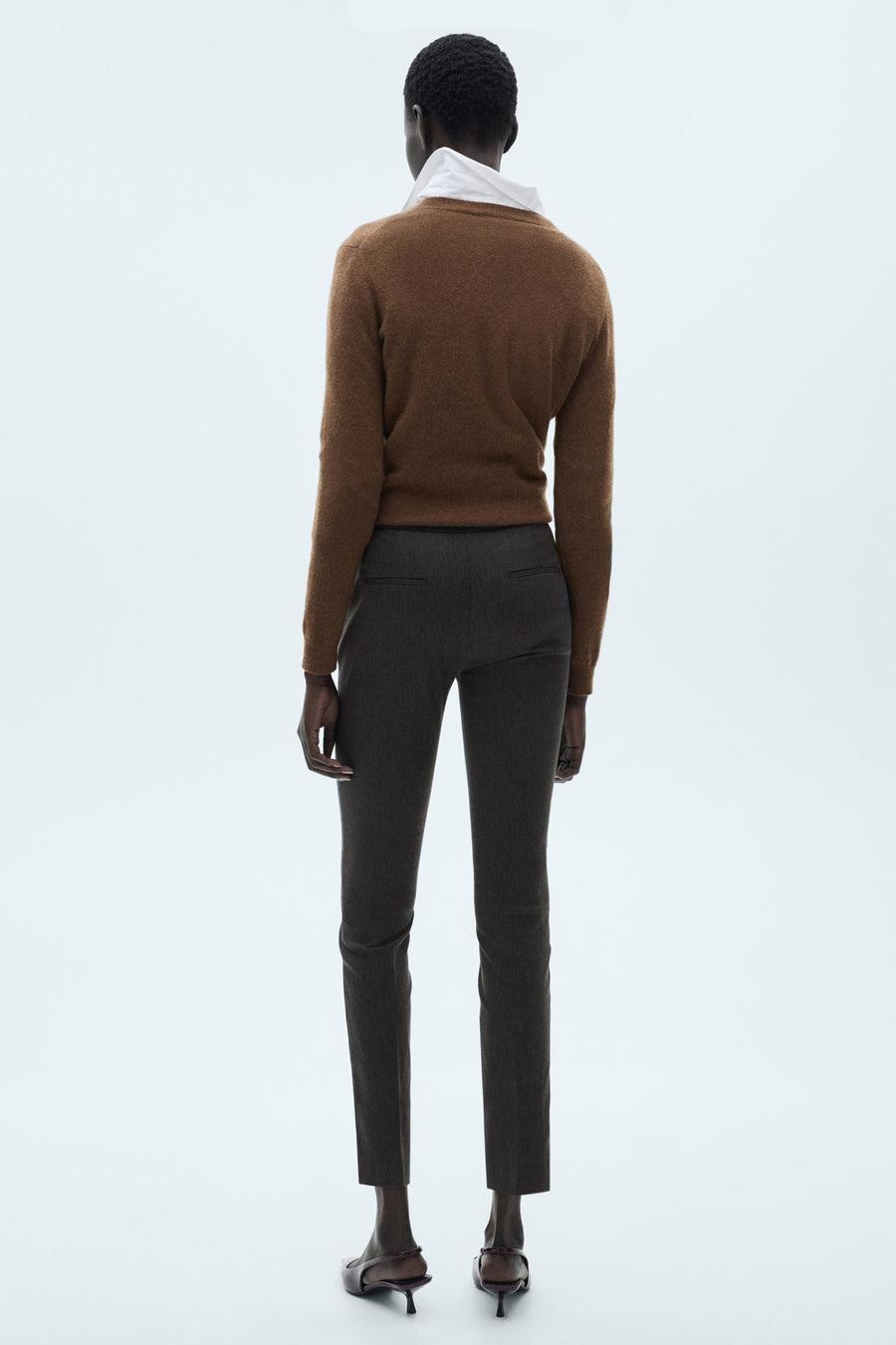 Pantalon gris de MANGO, coupe cigarette, porté avec un pull marron et des escarpins bordeaux.