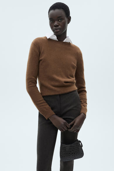 Grijze broek van MANGO, gedragen met een bruine trui en een wit overhemd, vastgehouden met een zwarte handtas.