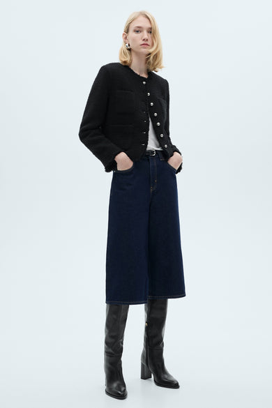 Gilet multicolore de MANGO, porté avec un jean ample bleu foncé, des bottes noires à talons et un t-shirt blanc.