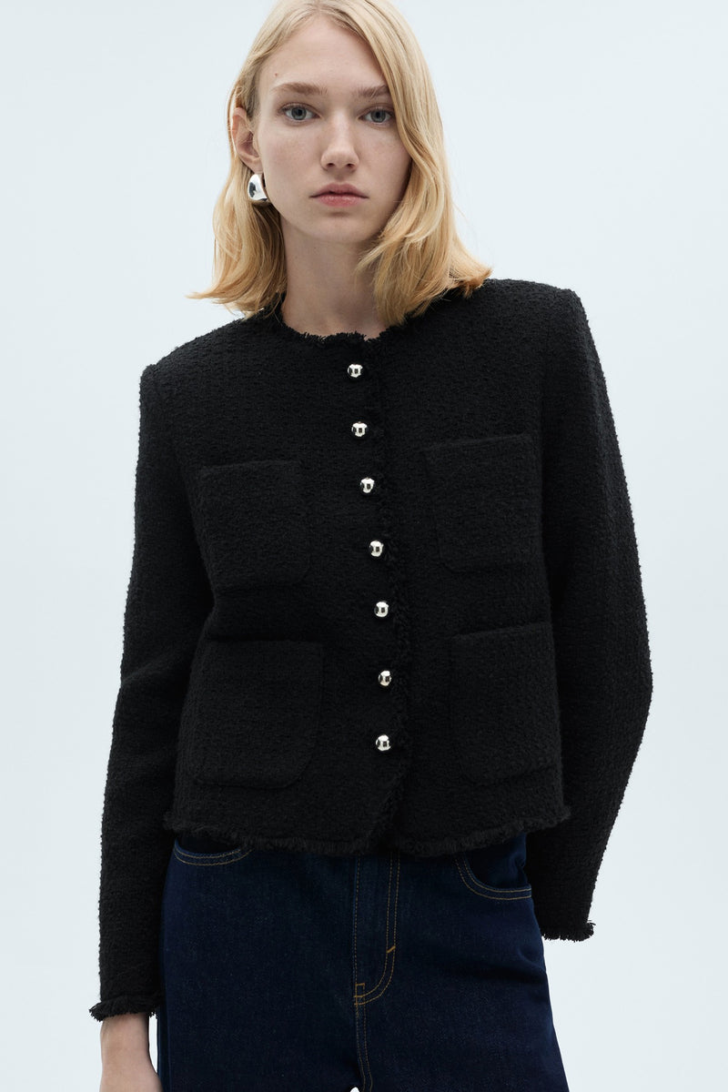 Gilet noir texturé par Mango, avec boutons argentés et poches plaquées, porté avec un jean foncé.
