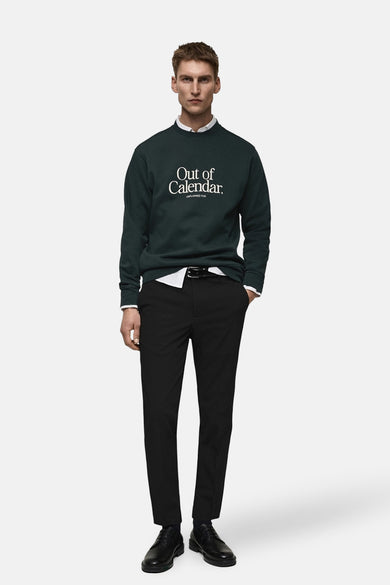 Pantalon de costume noir de MANGO, porté avec un pull vert et une chemise blanche.