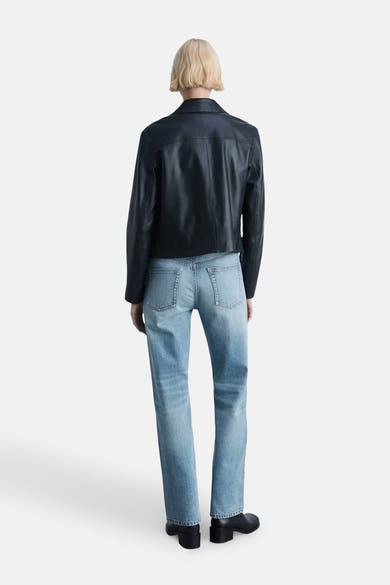 Jean droit bleu clair de MANGO, porté avec une veste en cuir noir et des bottines.