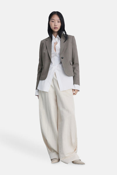 Blazer brun de MANGO, porté sur une chemise blanche et un pantalon ample beige.