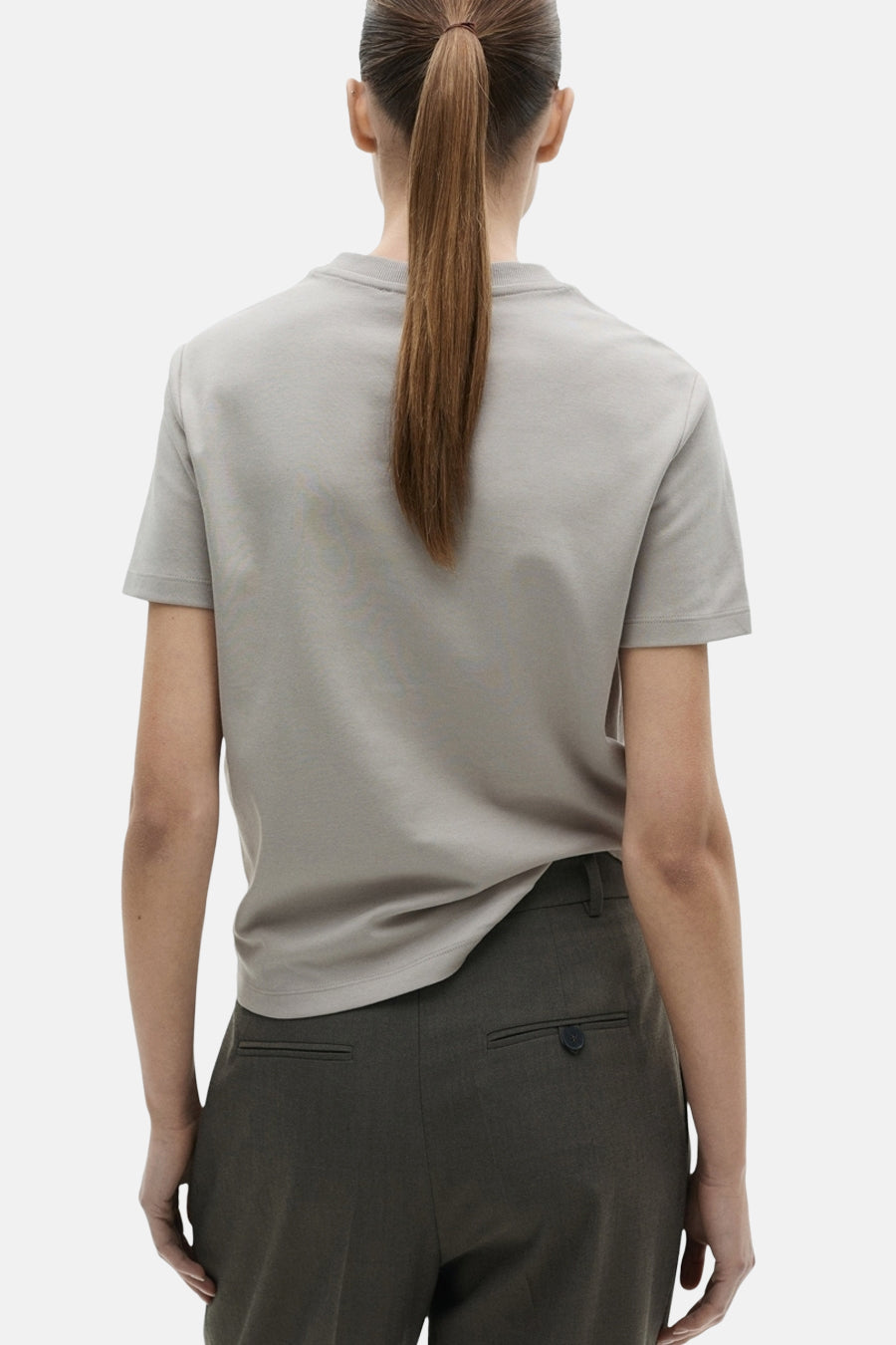 T-shirt à manches courtes gris de MANGO, porté avec un pantalon taille haute, vue de dos avec une queue de cheval.
