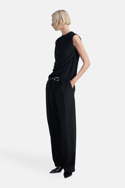 Zwarte mankante chemisier van MANGO, gedragen met een hoge taille pantalon en een riem en zwarte puntige schoenen.