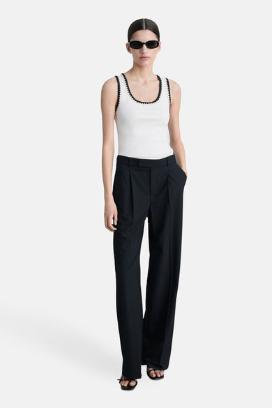 Ecru hemdje van MANGO, versierd met een contrasterende zwarte bies, gedragen met een wijde zwarte broek en sandalen.