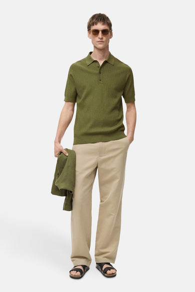 Polo vert à manches courtes de MANGO, en maille côtelée, porté avec un pantalon beige ample et des sandales noires.
