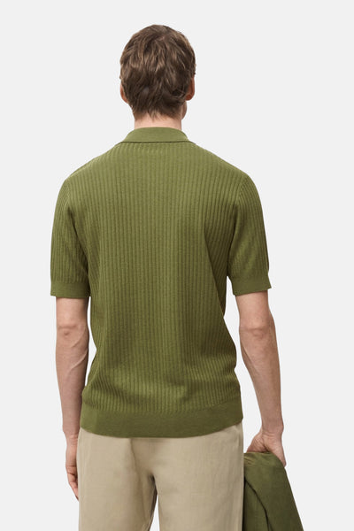 Polo à manches courtes vert de MANGO, en maille côtelée, porté avec un pantalon beige, vue de dos.
