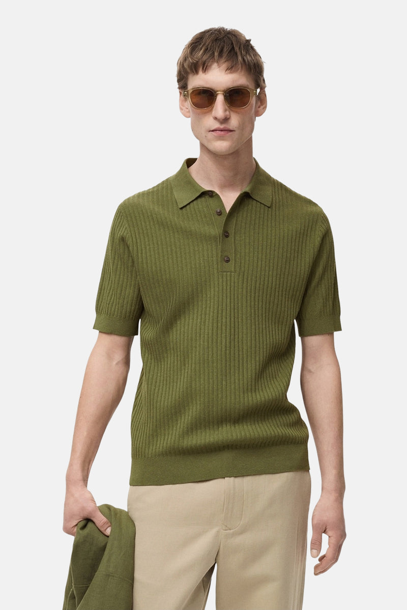 Polo vert côtelé à manches courtes de MANGO, porté avec un pantalon beige et des lunettes de soleil marron.