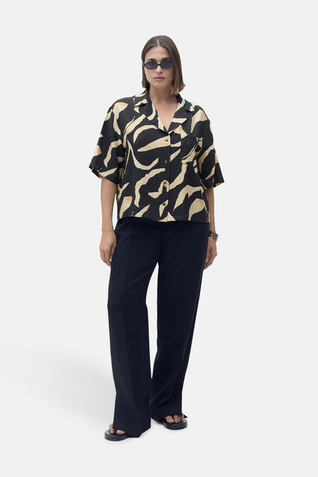 Zwart blouse met korte mouwen en abstract patroon, van MANGO, gedragen met een zwarte broek met hoge taille en een zonnebril.