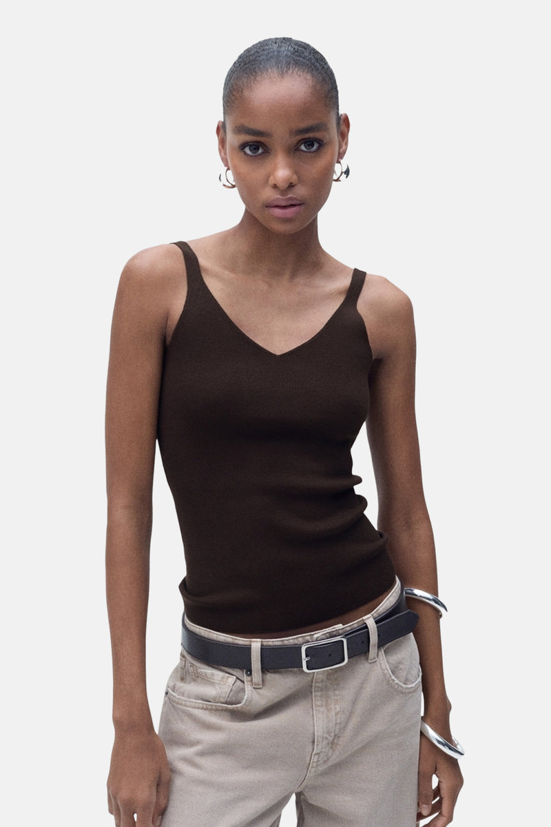 Débardeur brun de MANGO, à fines bretelles, porté avec un pantalon beige, une ceinture noire et des bracelets argentés.