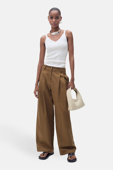 Débardeur blanc de MANGO, porté avec un pantalon marron ample et des sandales noires.