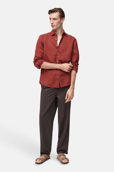 Rood overhemd met lange mouwen van MANGO, gedragen met een wit T-shirt en een bruine broek met sandalen.