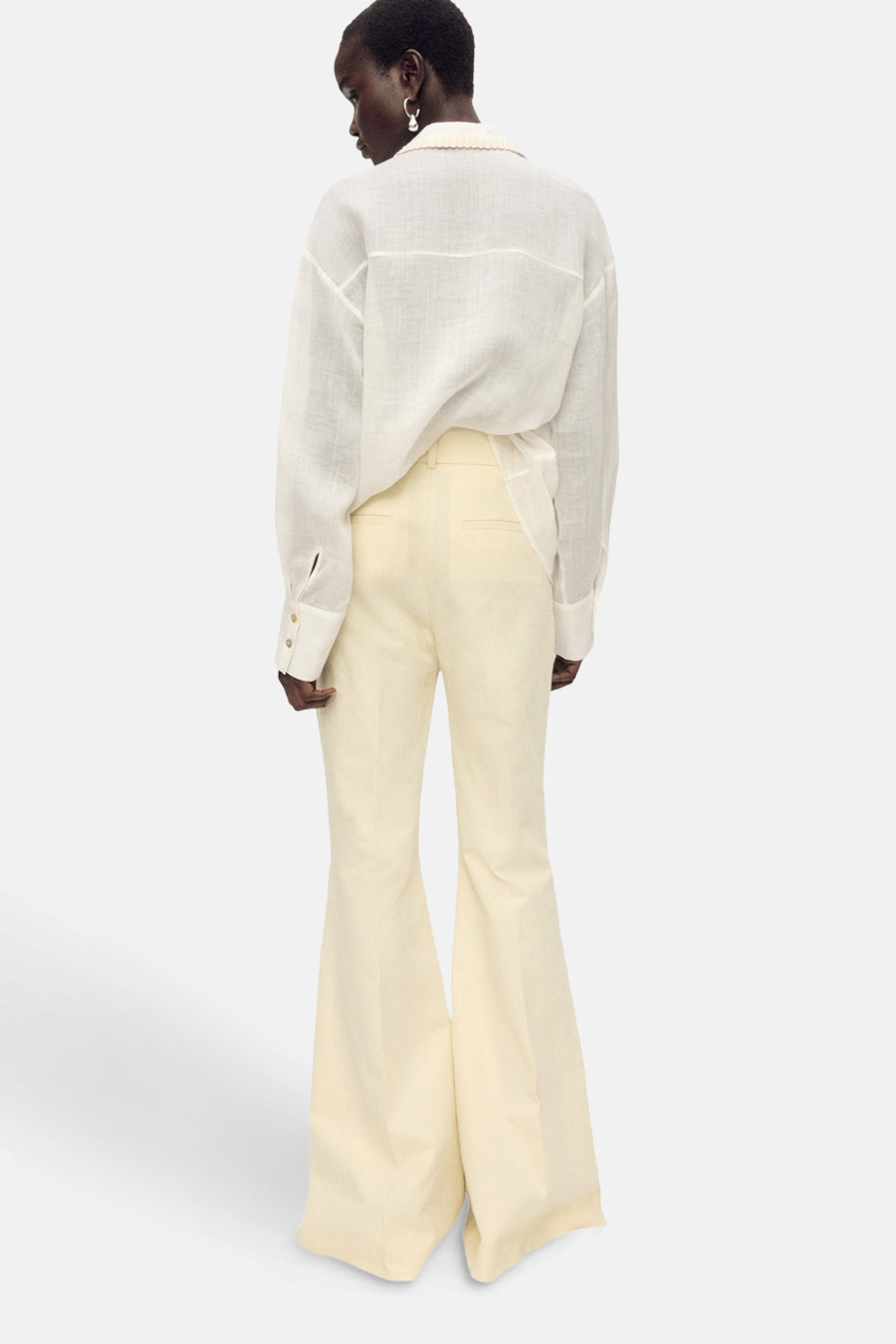 Wit overhemd met lange mouwen van MANGO, gedragen met een uitlopende broek en oorbellen.