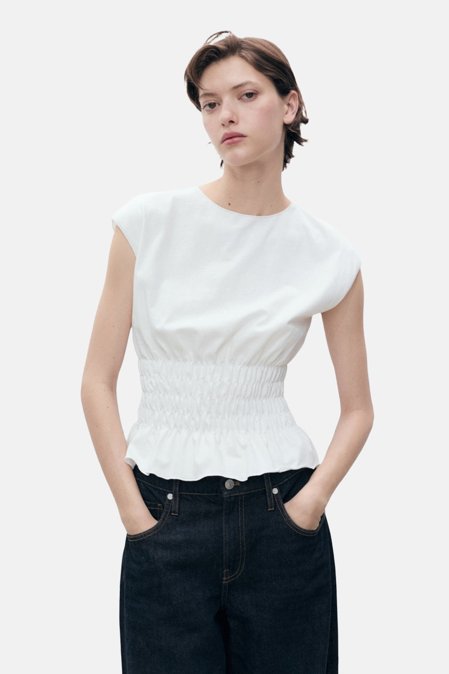 Wit mouwloos topje van MANGO, met geplooide taille en gedragen met een donkerblauwe jeans.