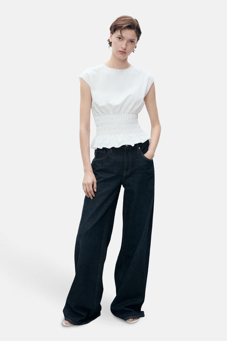 Wit mouwloos topje van MANGO, met smocktaille en volant, gedragen met een wijde jeans.