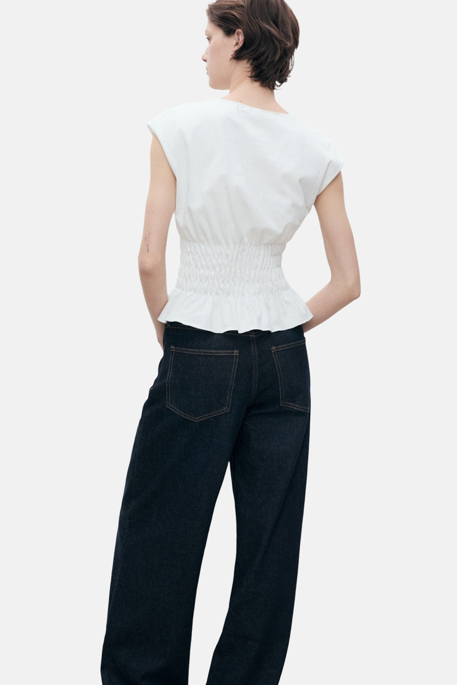 Wit mouwloos topje van MANGO, met geplooide taille en gedragen met een donkere spijkerbroek.