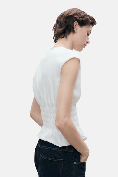 Wit mouwloos topje van MANGO, met een smocktail en gedragen met een donkerblauwe jeans.